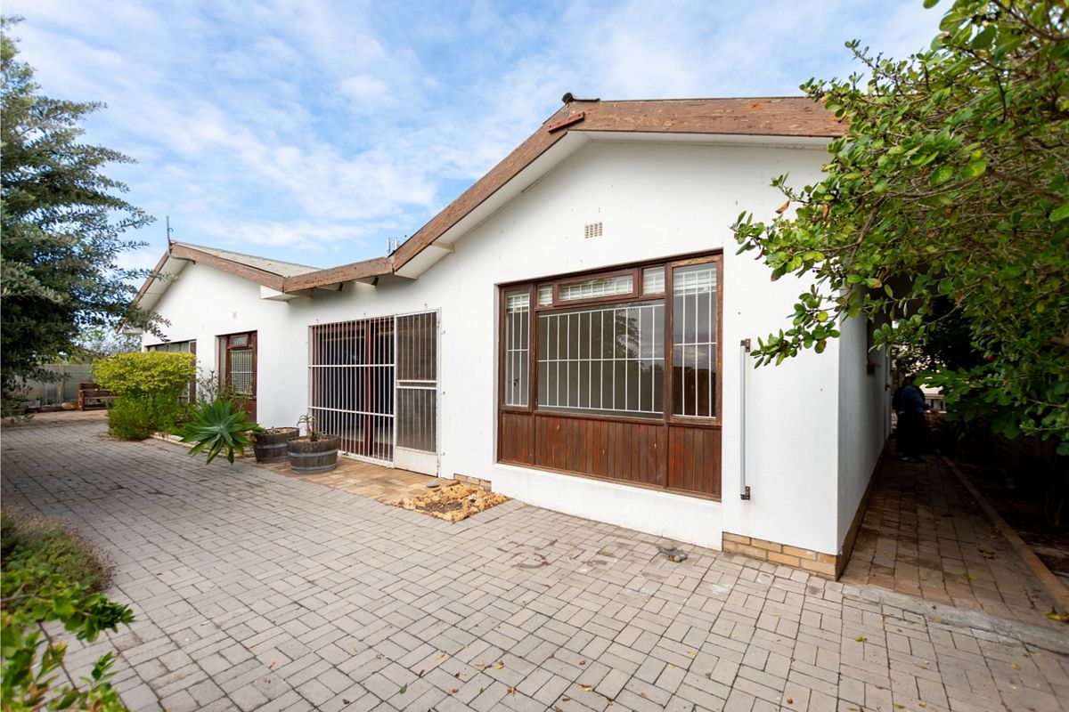 Rear exterior view of the house featuring a paved patio area, security bars on windows, and timber window frames.