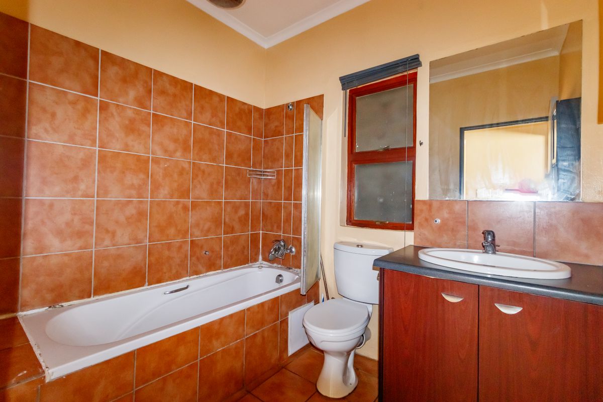 A functional bathroom featuring a bathtub, toilet, and vanity cabinet with a basin, finished with terracotta-style wall tiles.