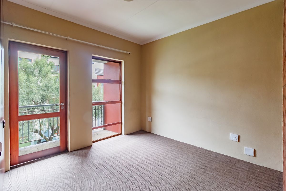 An empty bedroom featuring carpet flooring, neutral wall paint, and direct access to a small balcony through a timber-framed door.