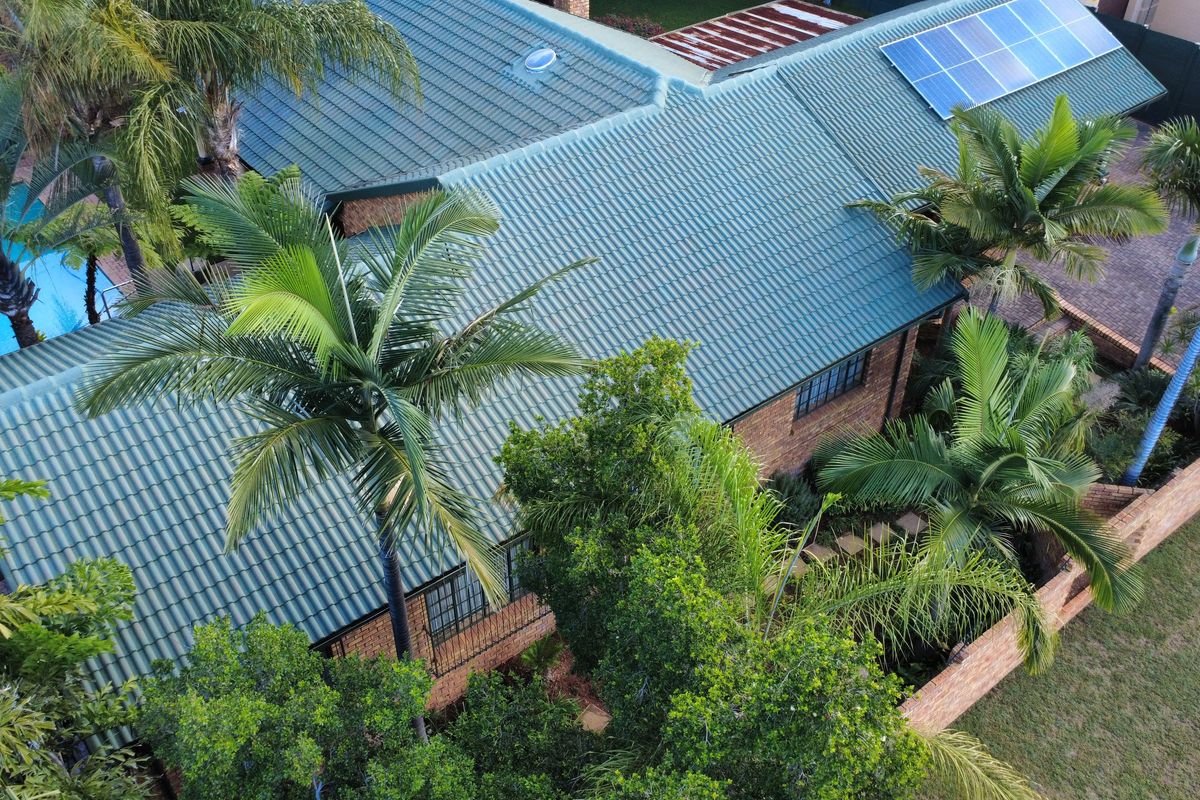 Aerial view of the property featuring a tiled roof with integrated solar panels, brick exterior, and a private swimming pool.