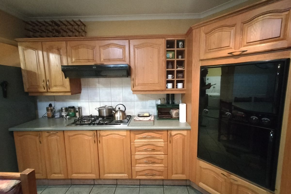 A functional kitchen featuring traditional wooden cabinetry, a gas hob with extractor fan, built-in oven, and tiled flooring.