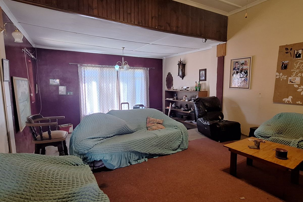 Spacious living room featuring a large open-plan layout, carpeted flooring, and a prominent ceiling beam, offering a blank canvas for modernization.