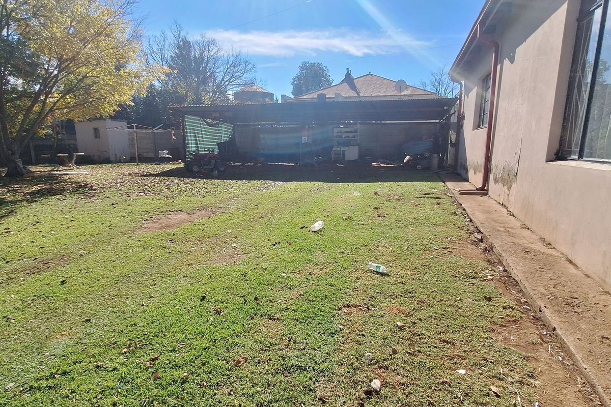 A spacious rear garden area featuring a large lawn, a detached carport structure, and direct access to the side of the main house.