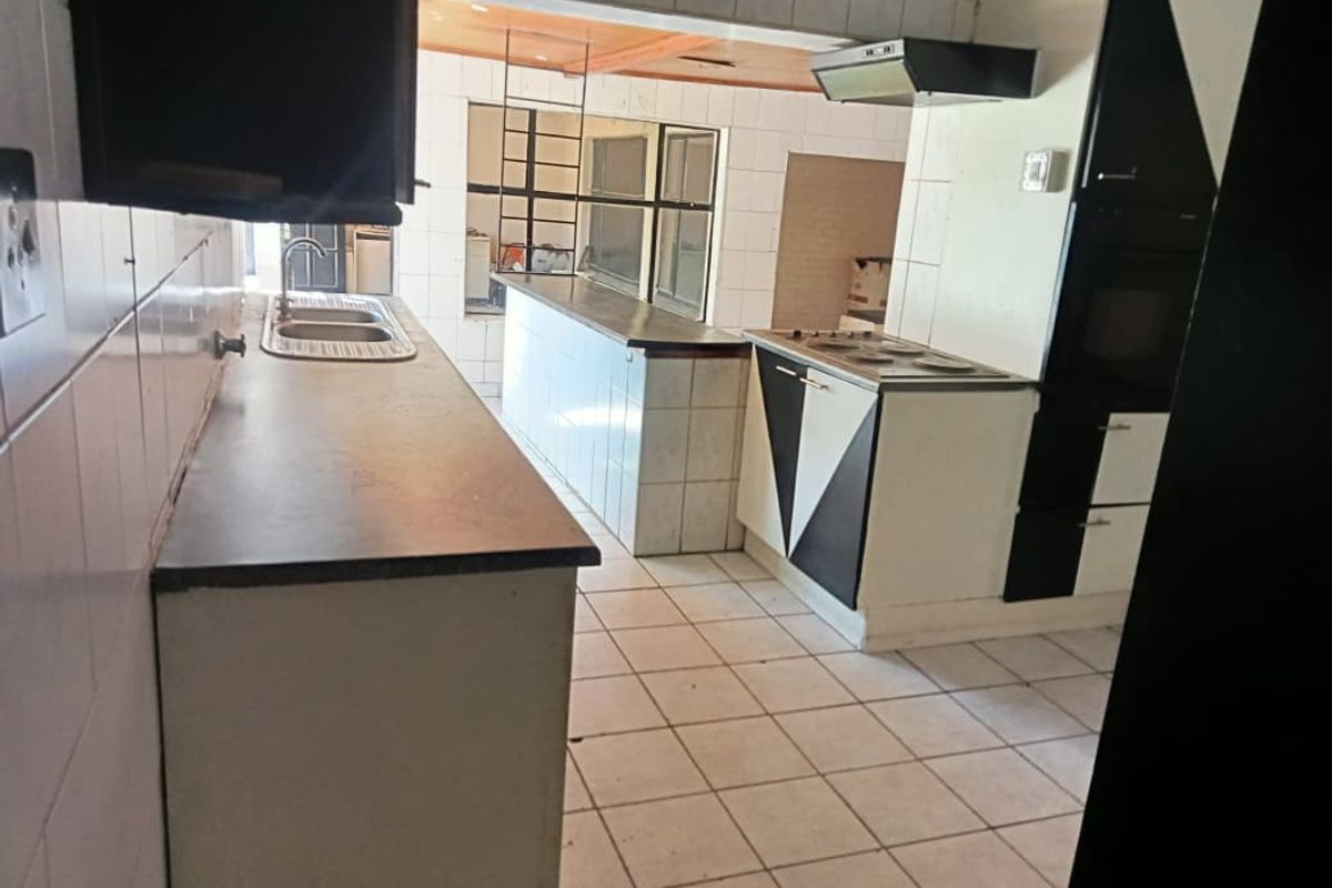 A dated kitchen featuring built-in cabinetry, a hob, an extractor fan, and a double bowl sink with tiled splashbacks and flooring.