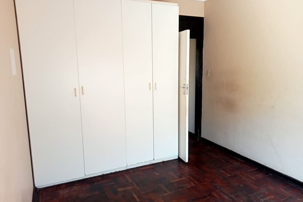 A bedroom featuring parquet flooring and a large built-in wardrobe, requiring cosmetic updates to the walls and floor finish.