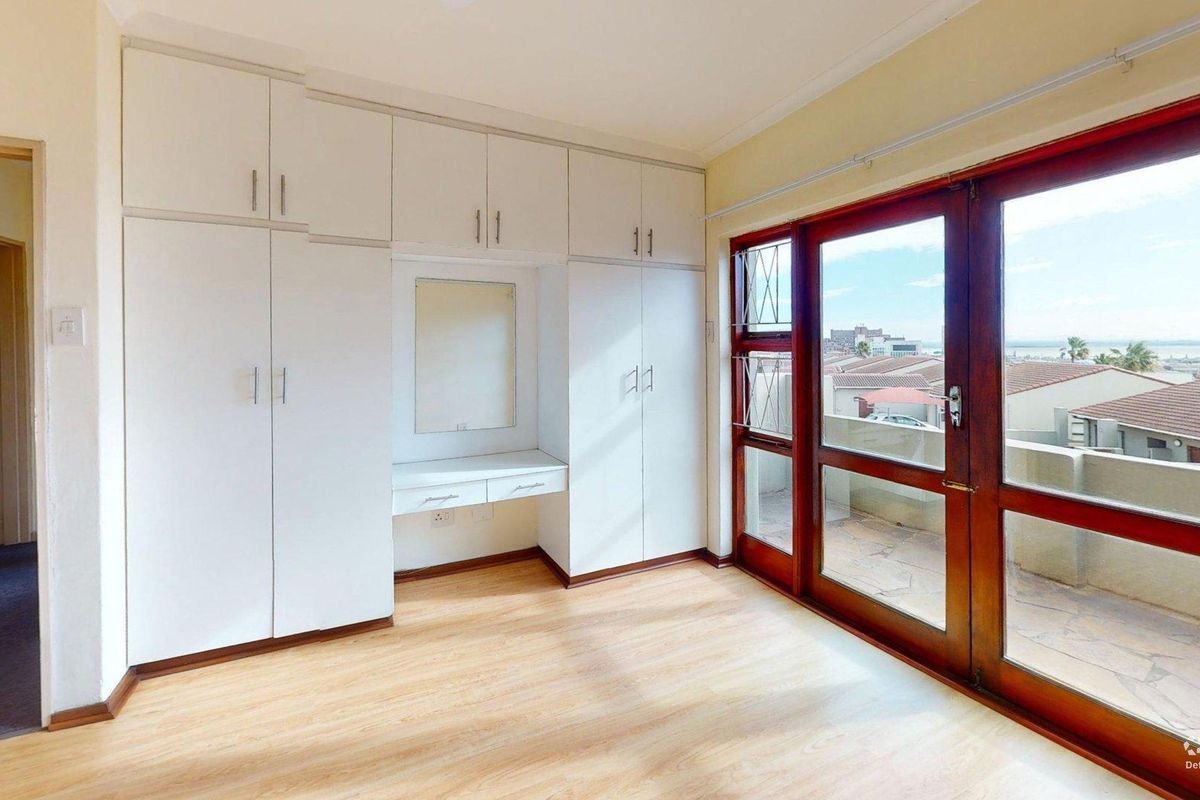 Bright bedroom featuring extensive built-in cabinetry with integrated vanity, laminate flooring, and large timber-framed glass doors opening onto a private balcony.