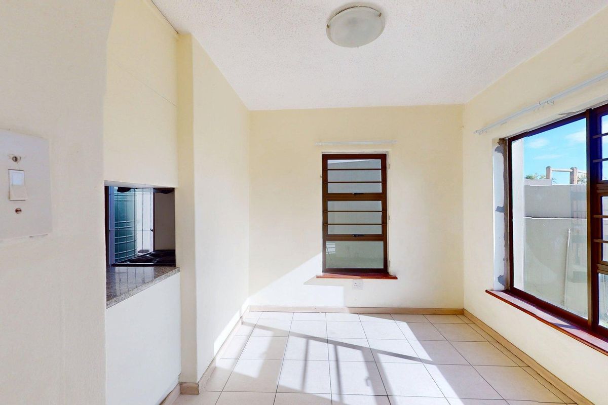 An empty kitchen area featuring tiled flooring, granite countertops, and aluminium windows with security bars, awaiting modern updates and finishes.