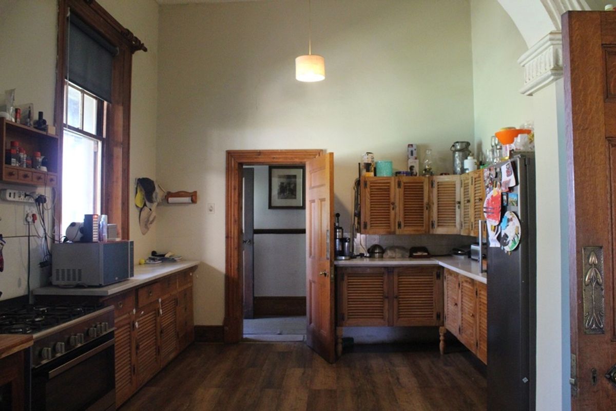 A traditional kitchen featuring wooden louvered cabinetry, a built-in gas stove, and high ceilings with original timber door frames.