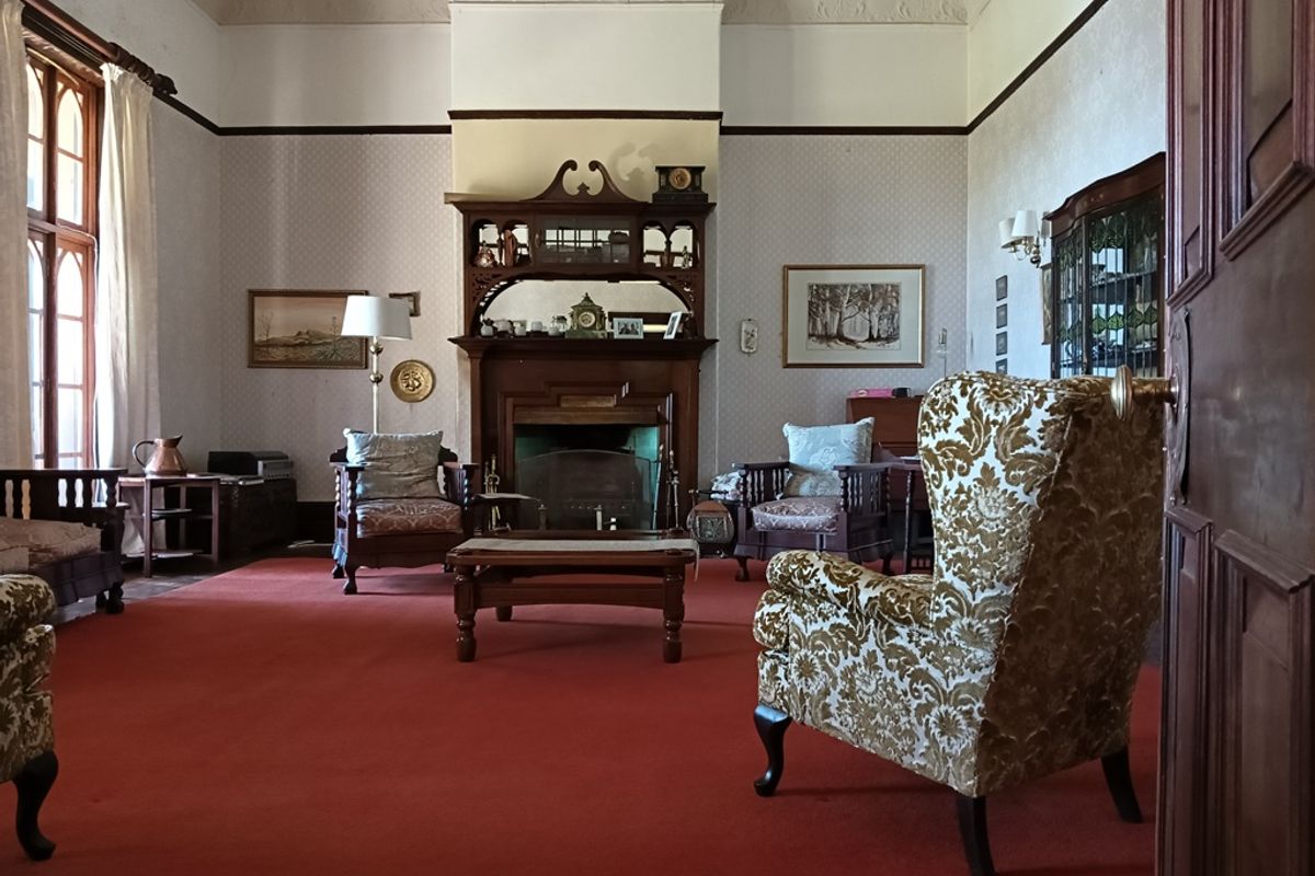 Spacious living room featuring a traditional fireplace with an ornate wooden mantelpiece, high ceilings with decorative cornicing, and large arched windows.