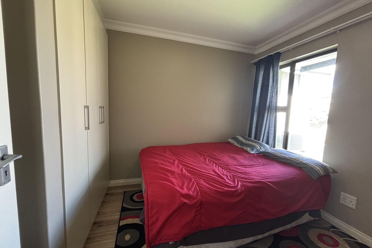 A bedroom featuring built-in cupboards, laminate flooring, and a sliding window with natural light.