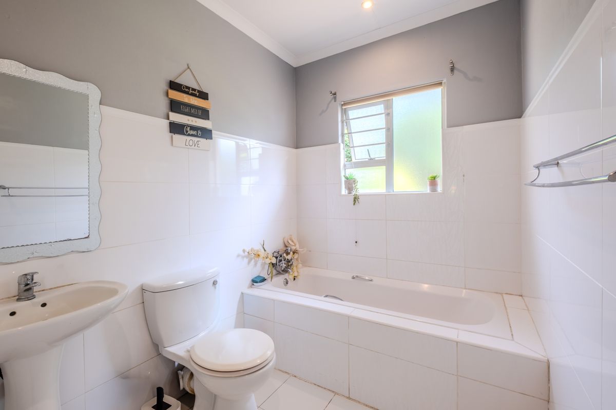 A functional bathroom featuring a pedestal basin, a standard toilet, and a tiled bathtub with a window for natural light.