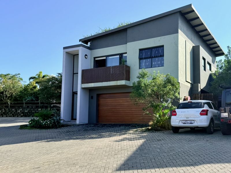 Front elevation of a modern double-storey townhouse featuring a timber garage door, paved driveway, and an upper-level balcony.