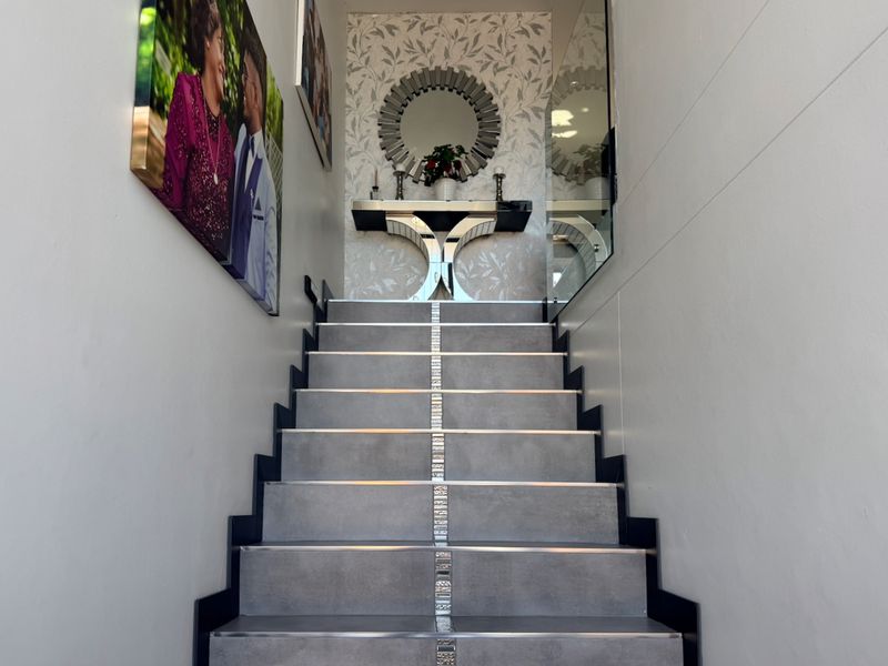 A well-maintained interior staircase featuring modern grey tiled treads with metallic accents and decorative wallpaper, leading to an upper landing area.