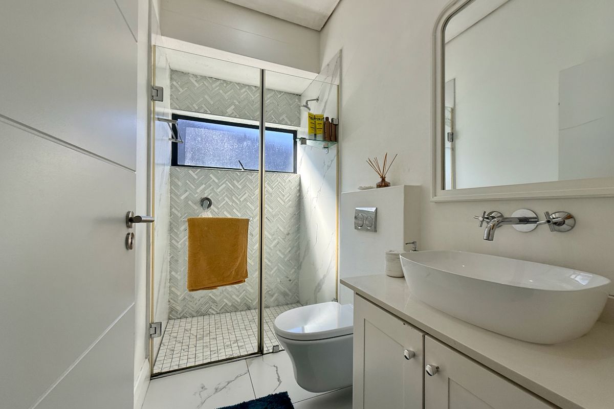 Modern bathroom featuring a glass-enclosed shower with herringbone tiling, a wall-mounted toilet, and a sleek vanity with a vessel sink.