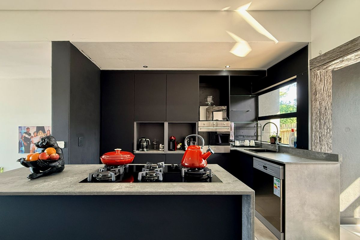 Modern kitchen featuring dark cabinetry, stone countertops, a central island with a gas hob, and integrated appliances.
