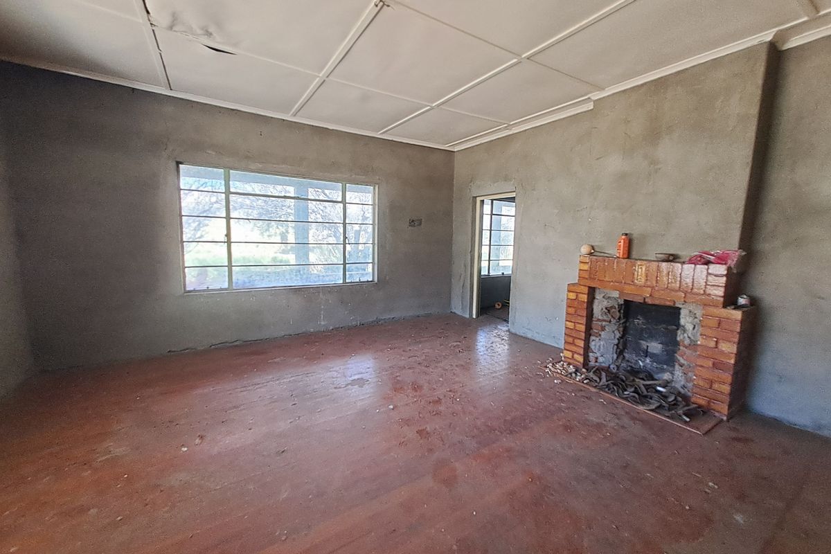 An empty living room featuring a brick fireplace, large window, and unfinished wall surfaces, offering a blank canvas for renovation.