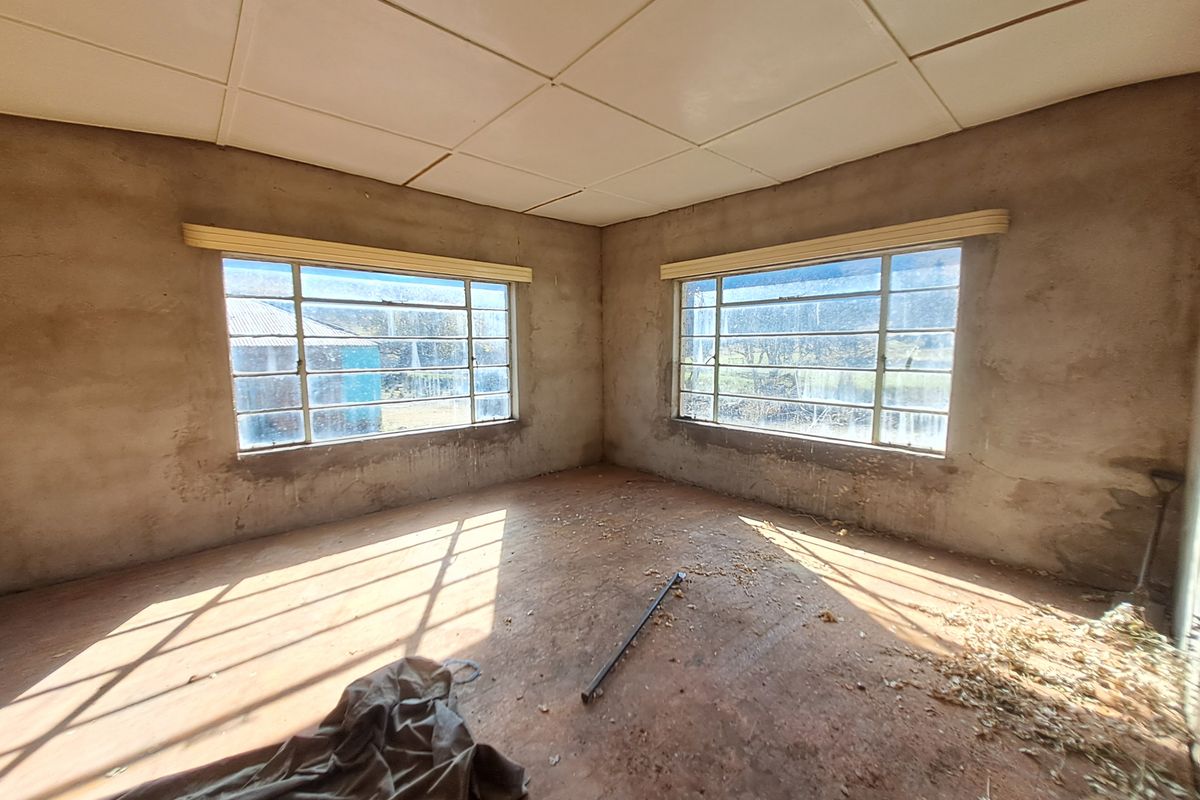 An unfinished interior room featuring exposed plaster walls, large metal-framed windows, and a drop ceiling, offering a blank canvas for renovation.