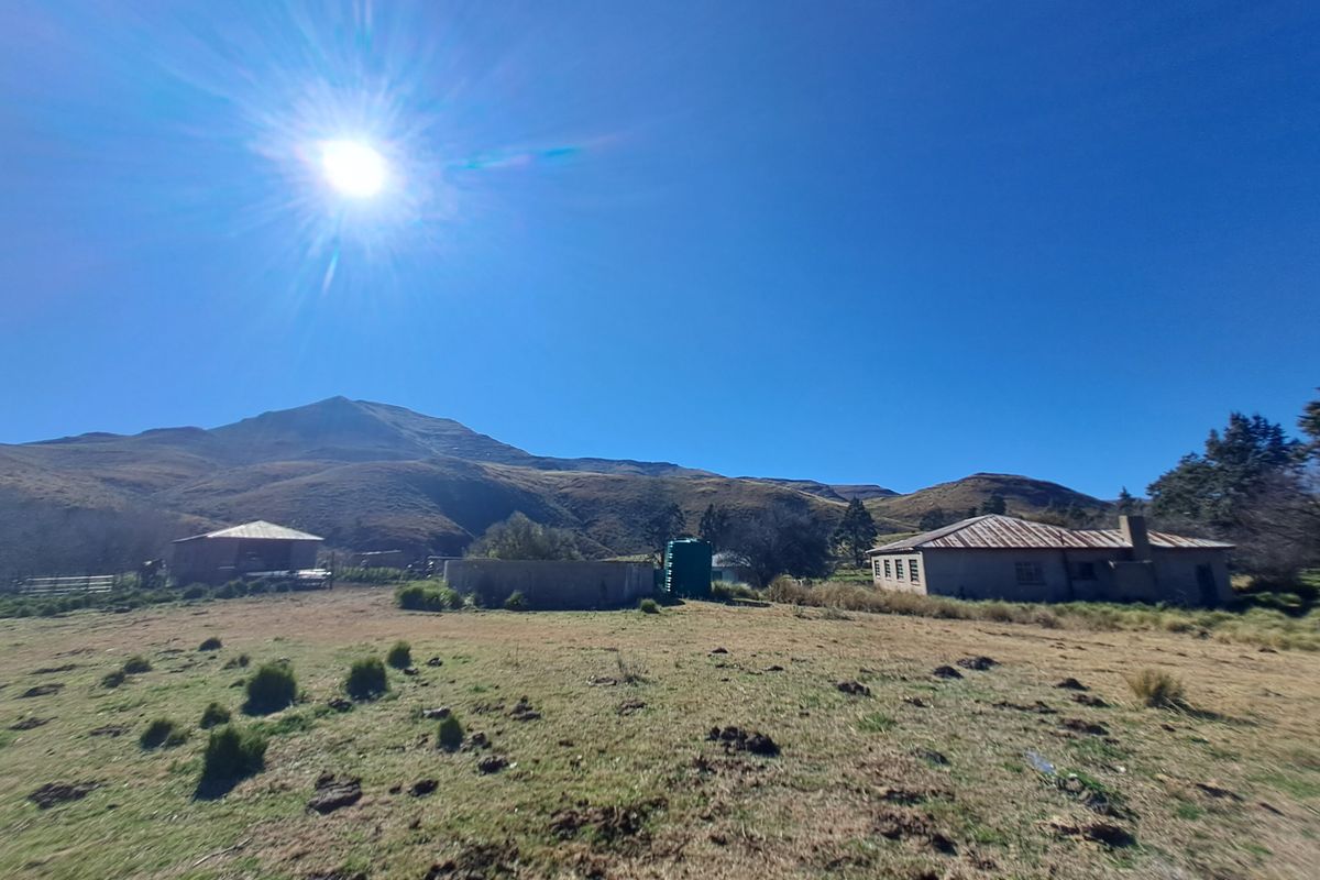Wide angle view of the farm property featuring multiple outbuildings, a water tank, and expansive mountain landscape views under a clear sky.