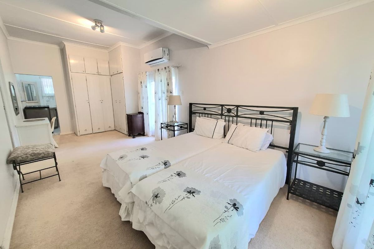 Spacious bedroom featuring built-in cupboards, neutral carpeting, and a wall-mounted air conditioning unit.