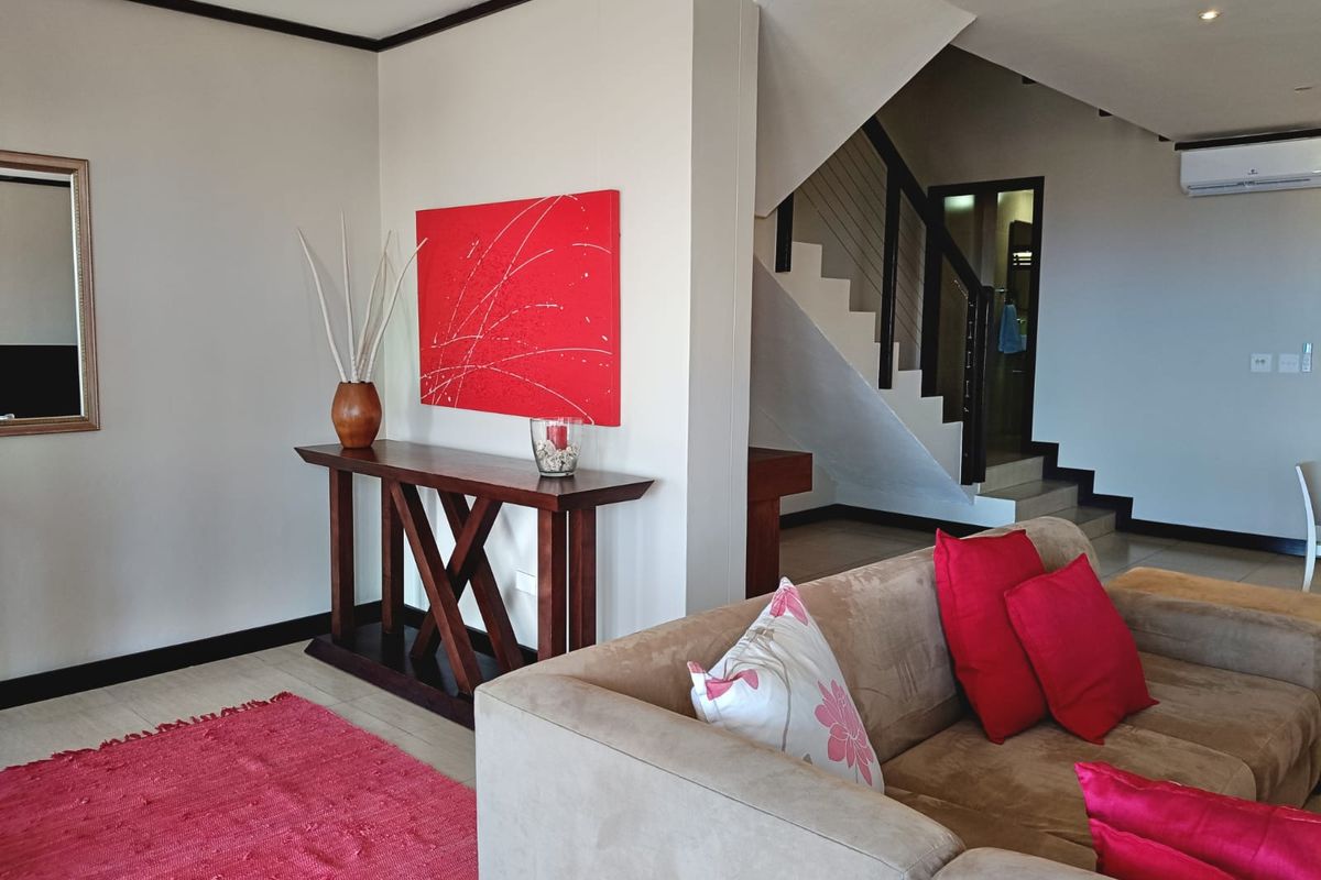 Open-plan living area featuring tiled flooring, recessed lighting, and a staircase leading to the upper level, complemented by a wall-mounted air conditioning unit.