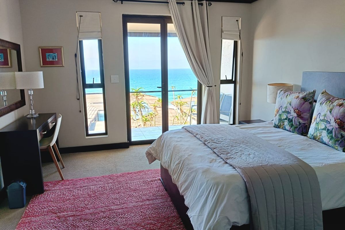 A well-maintained bedroom featuring carpeted flooring and a sliding glass door that opens to a balcony with ocean views.