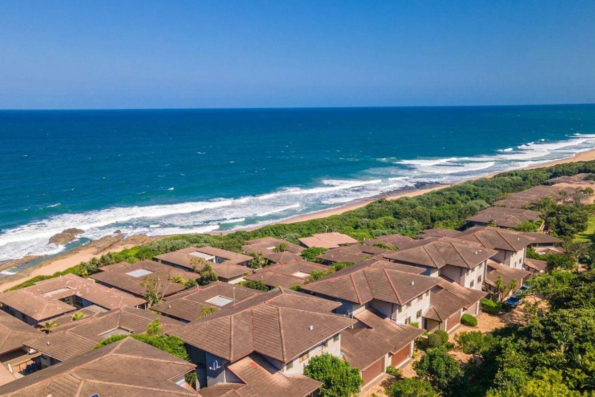Aerial view of a coastal townhouse complex situated directly along the beachfront, showcasing the roof structures and proximity to the ocean.