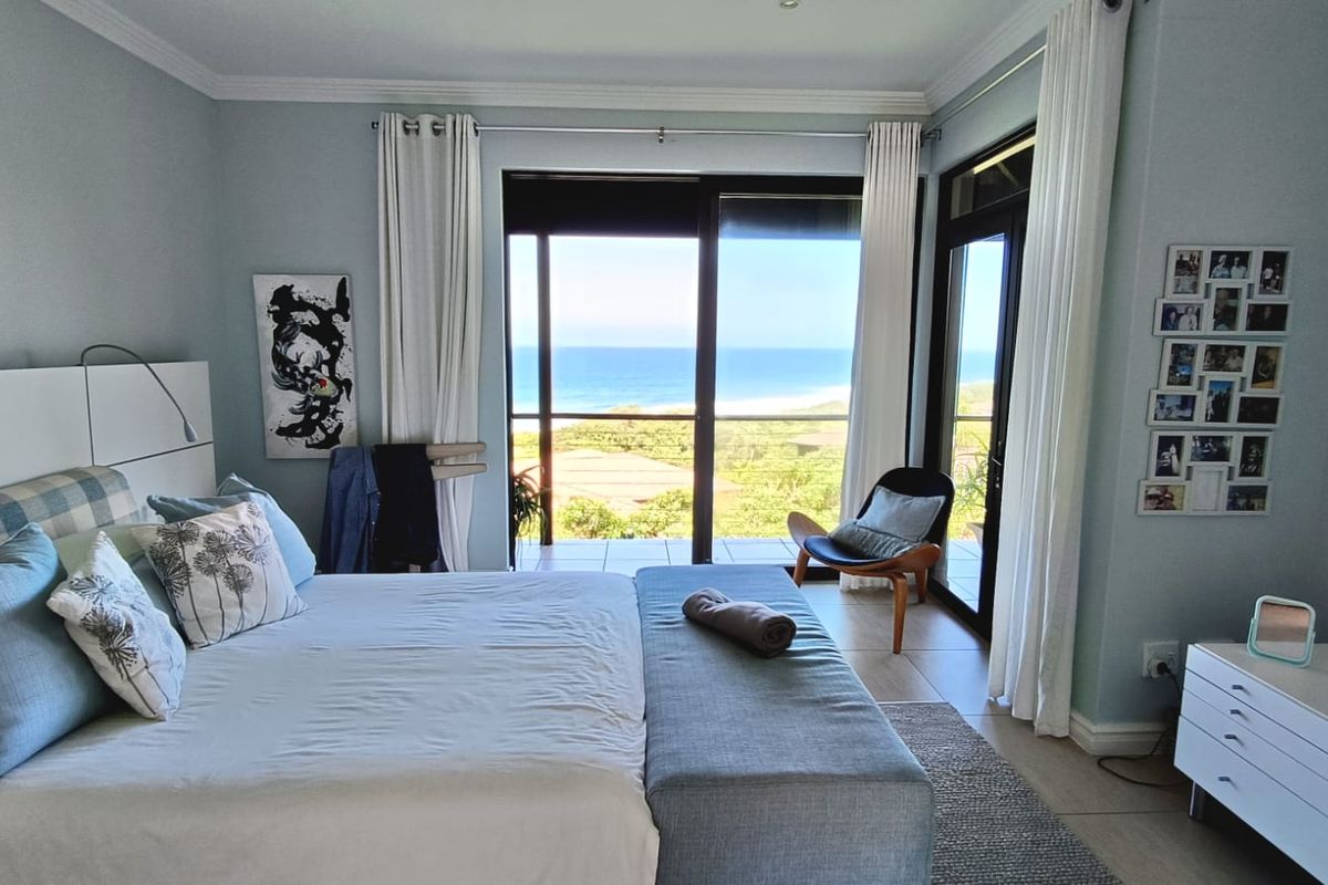 Spacious bedroom featuring large sliding glass doors that open to a balcony with expansive ocean and coastal views.