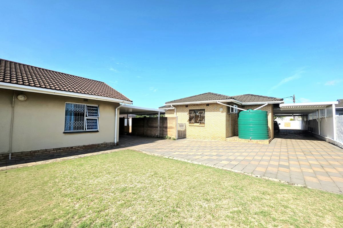 Rear exterior view of the property featuring a paved courtyard, carport, and a large water storage tank set against a well-maintained lawn.