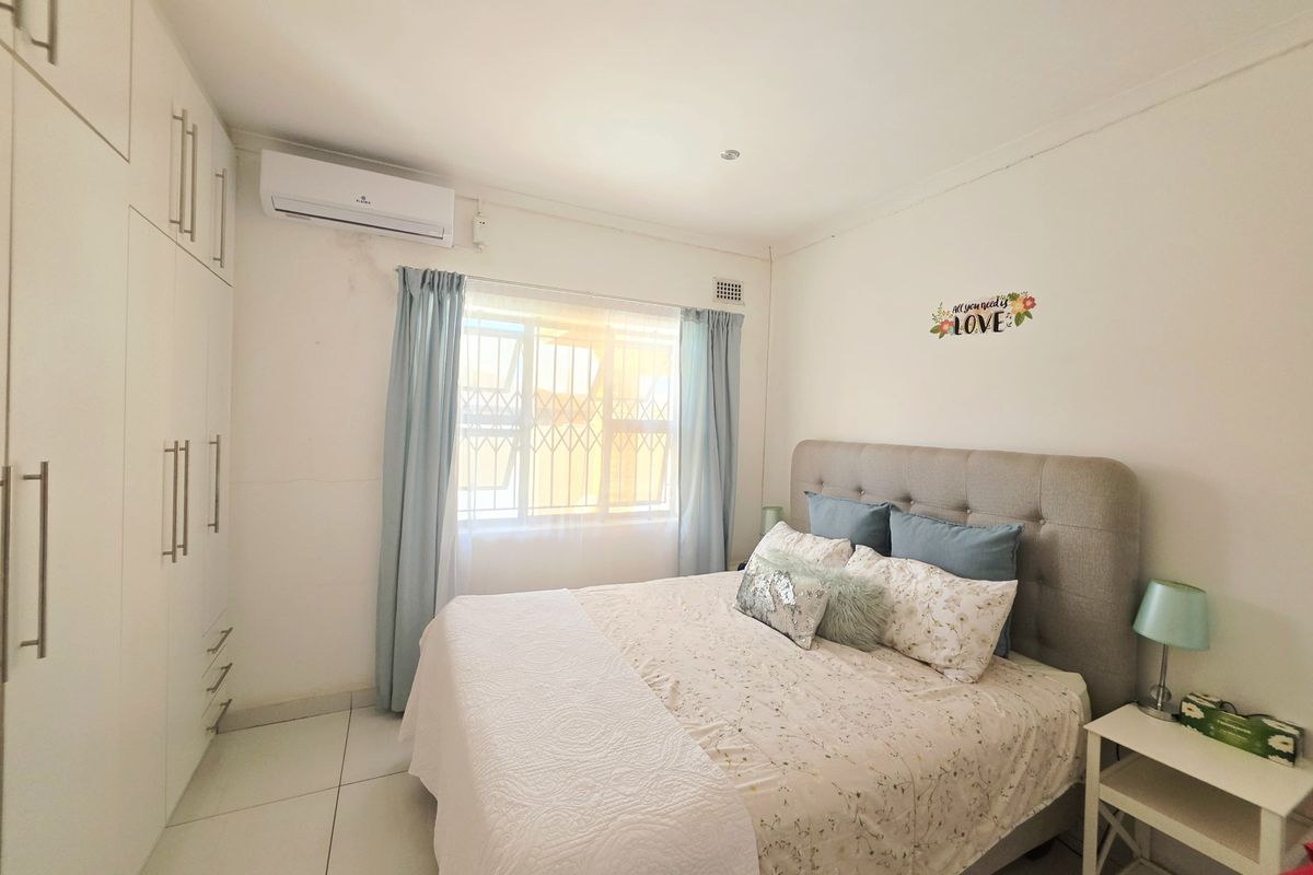 A well-maintained bedroom featuring built-in cupboards, tiled flooring, and a wall-mounted air conditioning unit for climate control.