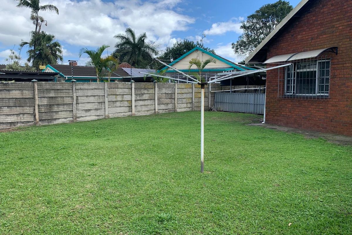 A spacious rear garden featuring a lawn, a rotary clothesline, and a brick exterior wall with security-fitted windows.