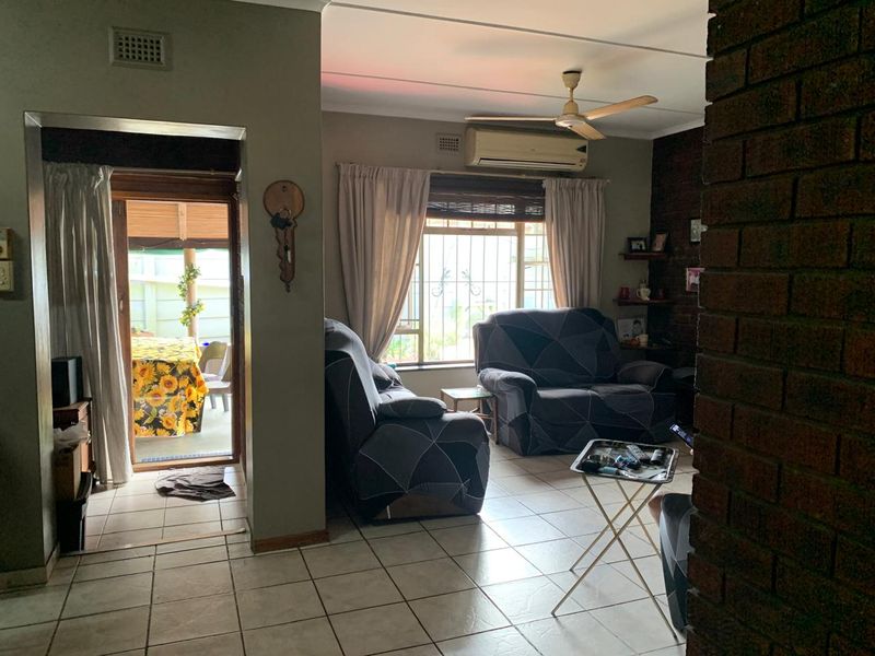 A living room featuring tiled floors, an exposed brick accent wall, a ceiling fan, and a split-system air conditioner, with access to an outdoor patio.
