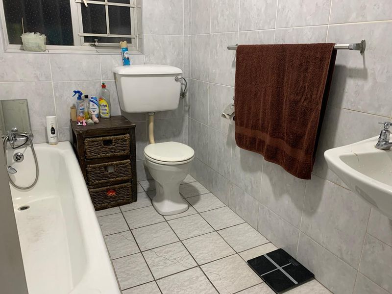 A functional bathroom featuring a bathtub, toilet, and washbasin with full-height wall tiling and tiled flooring.