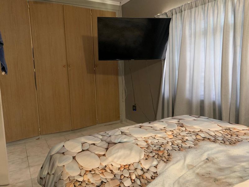 A bedroom featuring built-in wooden cupboards, tiled flooring, and window treatments.