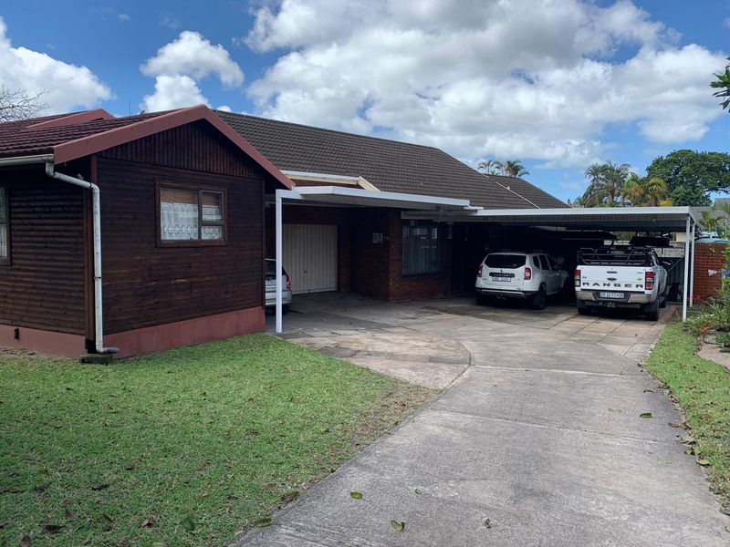 Front exterior view of the property featuring a concrete driveway, carport, garage, and a combination of brick and timber cladding.