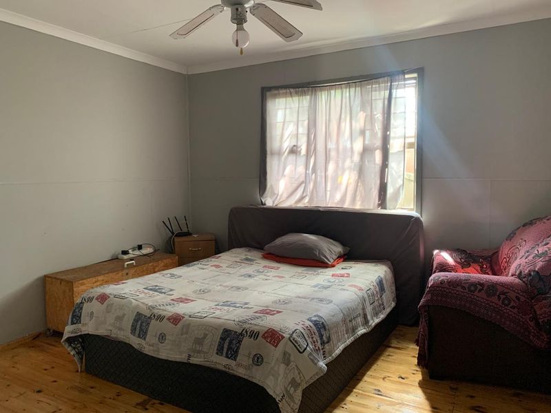 A bedroom featuring timber flooring, a ceiling fan, and visible wall paneling, offering a functional space with potential for cosmetic updates.