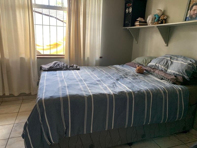 A functional bedroom featuring tiled flooring, a wall-mounted shelf, and a window fitted with security bars.
