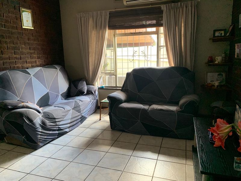 A living room featuring tiled flooring, an exposed brick feature wall, and a window fitted with security bars.