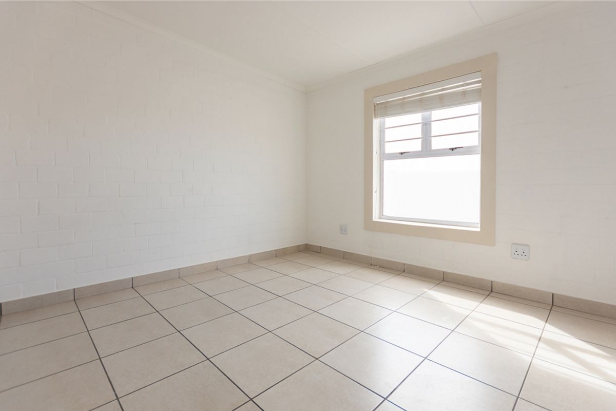 A bright, empty bedroom featuring neutral tiled flooring, painted brick walls, and a window with fitted blinds.
