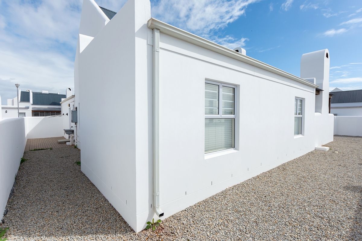 A clean, well-maintained rear exterior view of the property featuring white rendered walls, modern downpipes, and a gravel-surfaced side yard.