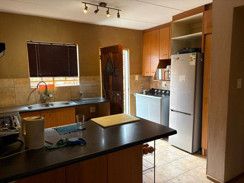 Functional kitchen featuring wooden cabinetry, laminate countertops, double basin sink, and tiled backsplash with direct access to the exterior.