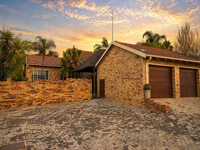 Front exterior view of a face brick townhouse featuring a double garage, paved driveway, and a combination of tiled and thatched roof sections.