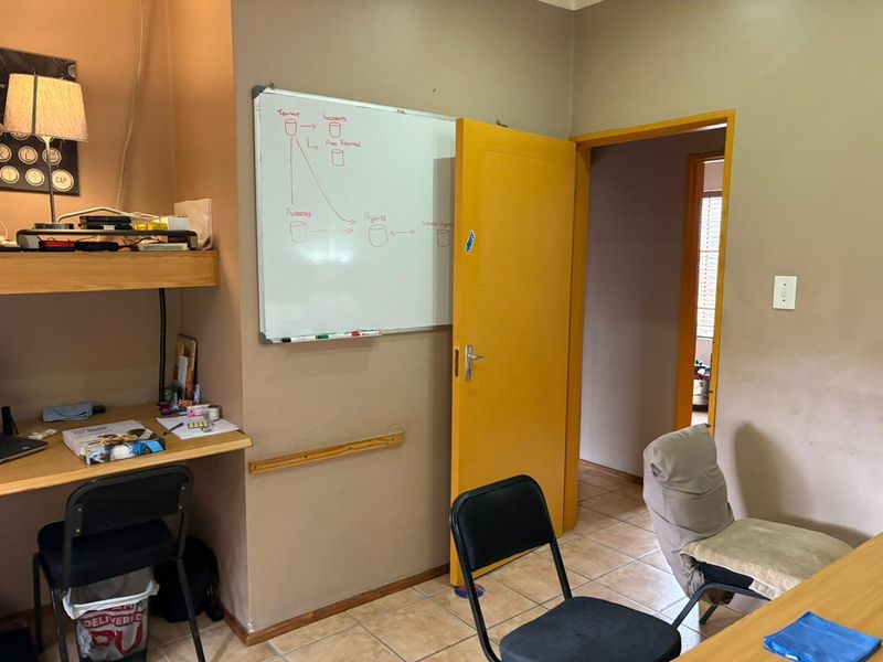 A functional home office space featuring tiled flooring, a built-in desk, and direct access to an adjoining room.