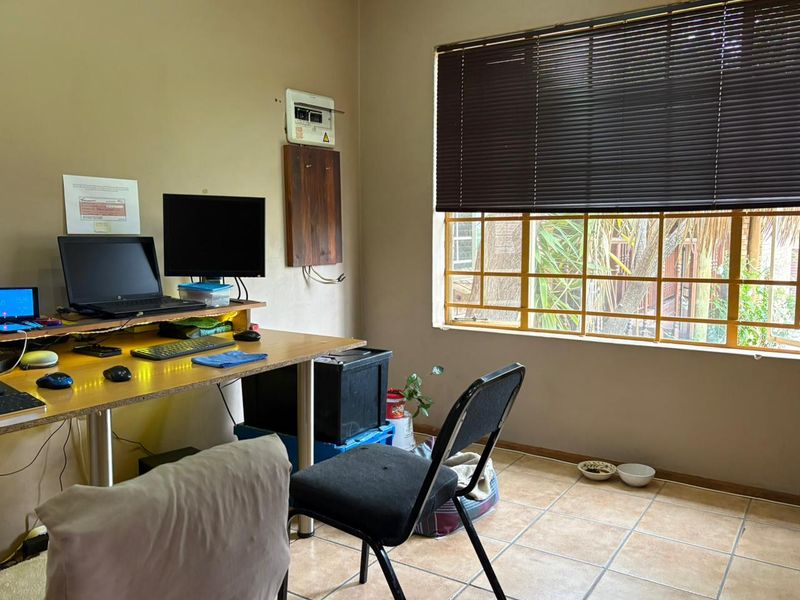 A functional home office space featuring tiled flooring, a window with security bars, and an accessible electrical distribution board.