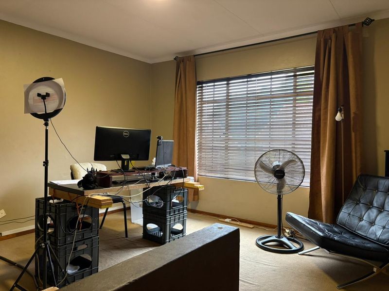 A functional home office space featuring carpeted flooring, window blinds, and curtain rails, providing a versatile area for work or study.