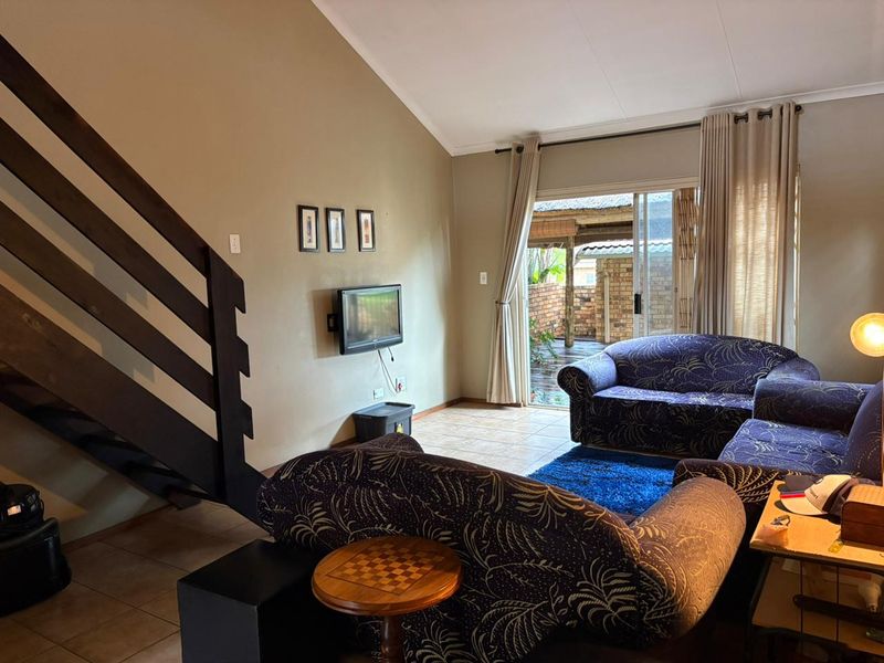 A living room featuring a staircase, vaulted ceiling, and sliding glass doors that provide access to an outdoor patio area.