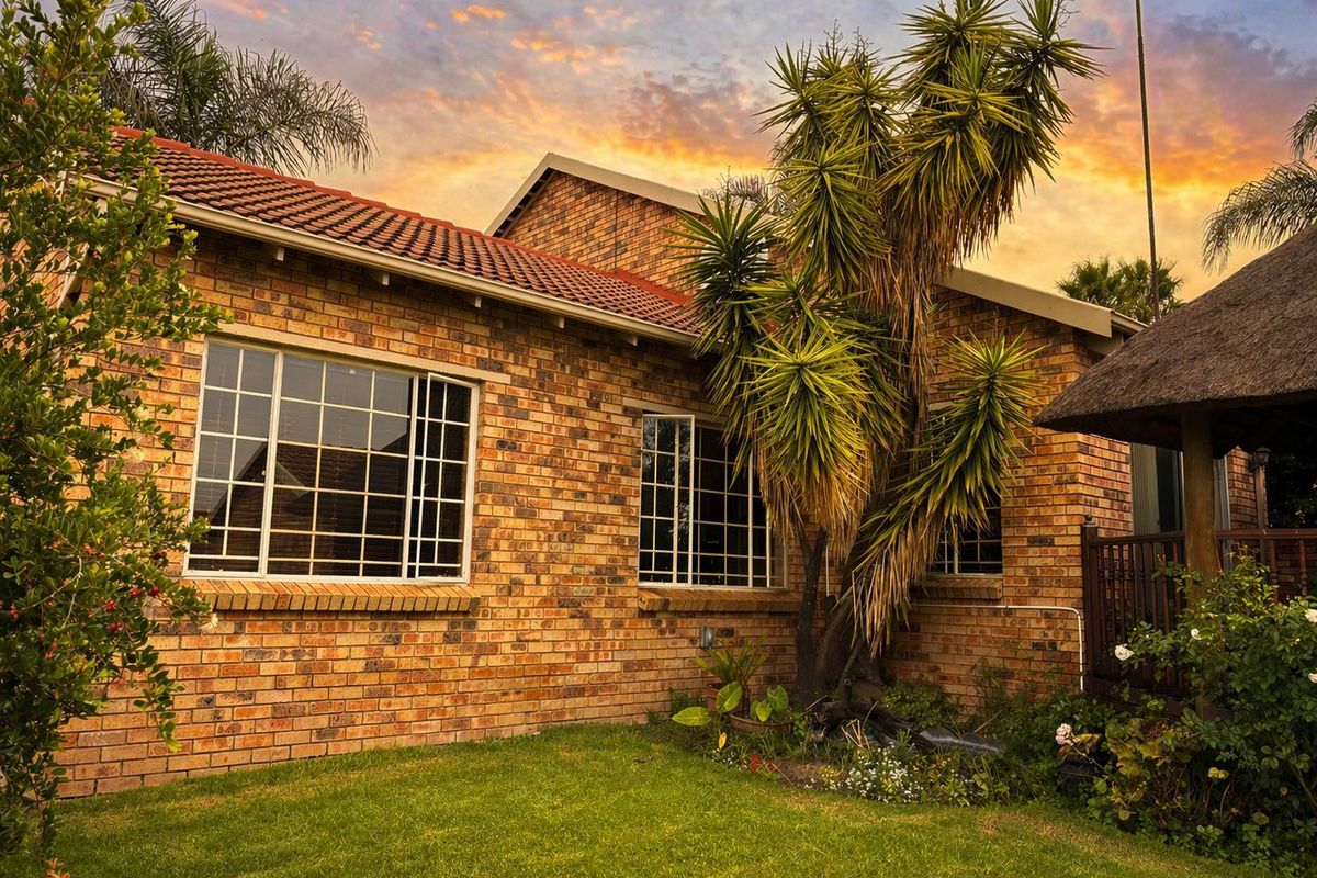 Rear view of the townhouse featuring a classic face brick facade, tiled roof, and an adjacent thatched lapa area set within a private garden.