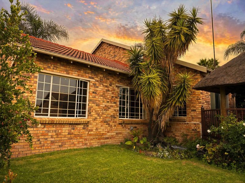 Rear view of the townhouse featuring a classic face brick facade, tiled roof, and an adjacent thatched lapa area set within a private garden.