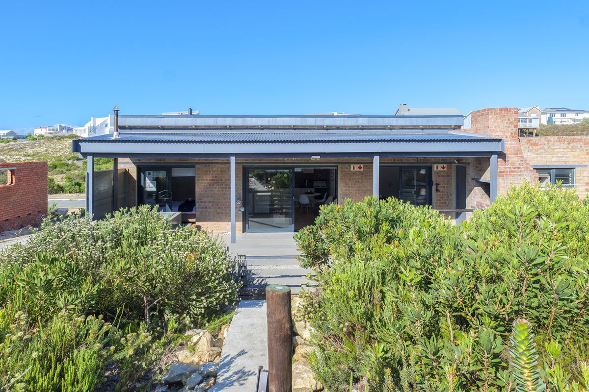Rear view of a modern brick house featuring a covered patio, sliding glass doors, and a built-in outdoor fireplace, set within a landscaped garden.
