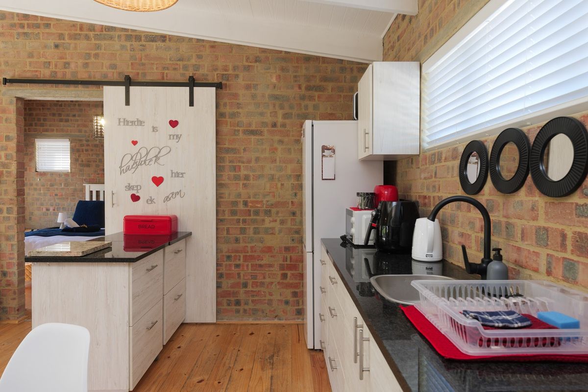 A functional kitchen featuring exposed brick walls, granite countertops, timber flooring, and a sliding barn door leading to an adjacent bedroom.