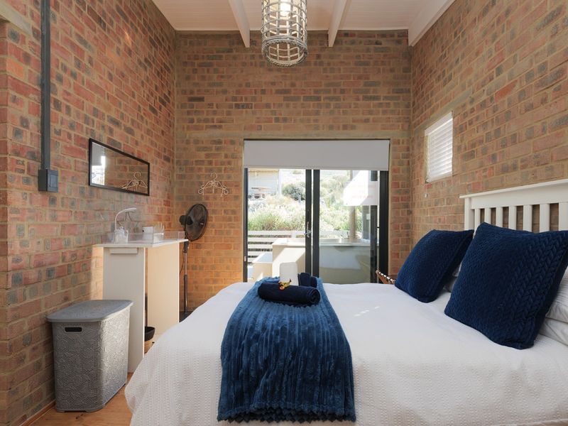 A cozy bedroom featuring exposed brick walls, timber ceiling beams, and direct access to an outdoor patio through sliding glass doors.